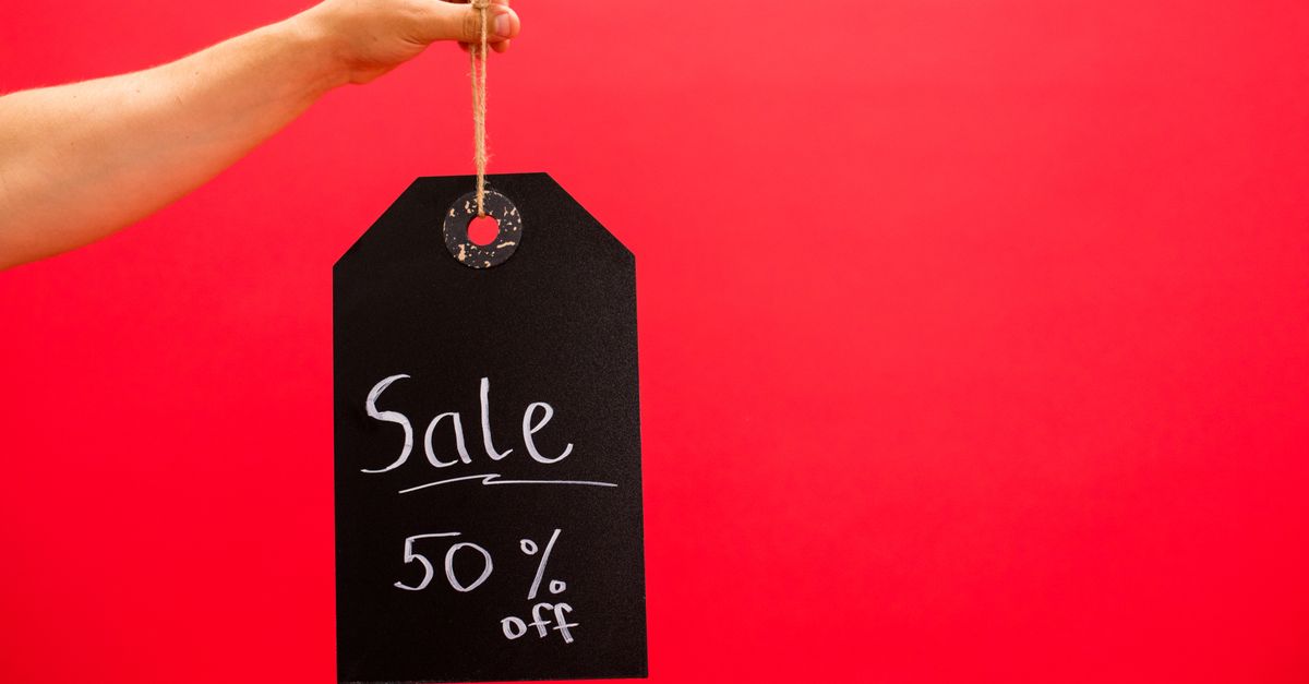 Hand holding a black sale tag with 50% off on a vibrant red background.